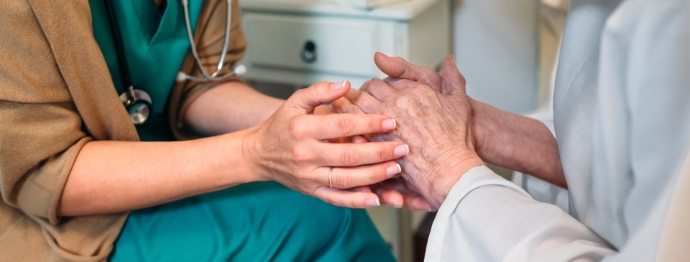 Female doctor giving encouragement to elderly patient by holding her hands